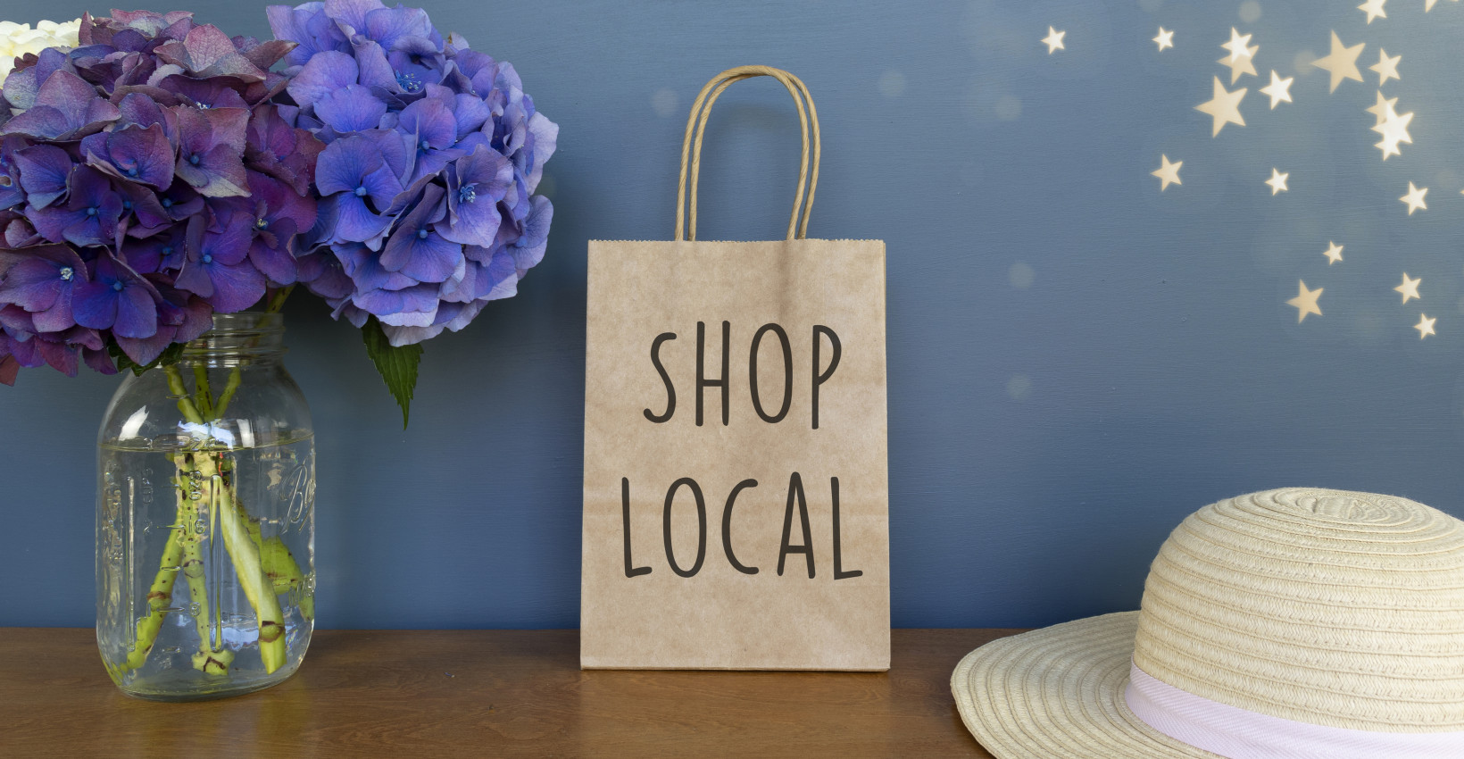 Shop local written on a paper bag with a hat and flowers.