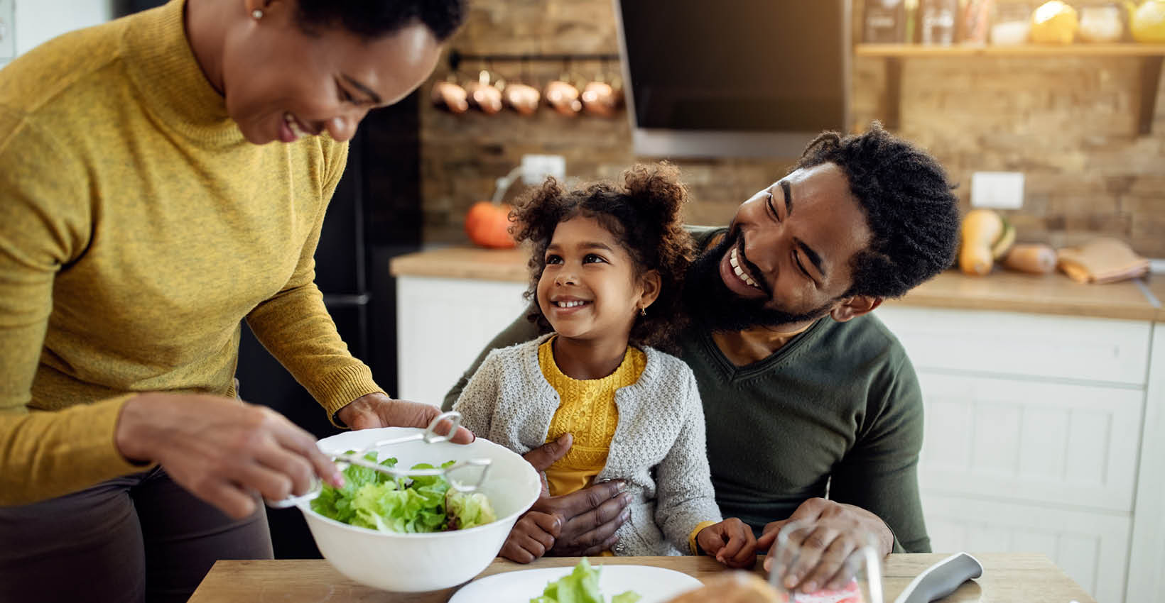 A mom serving salad to her husband and daughter