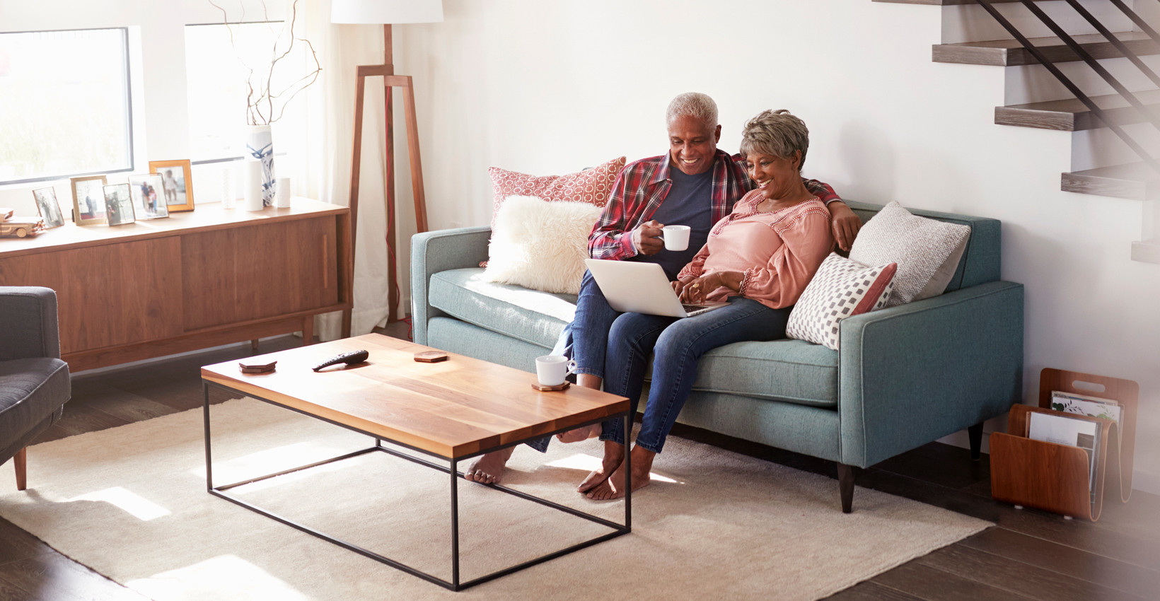 An elderly couple sitting on the couch looking at a laptop
