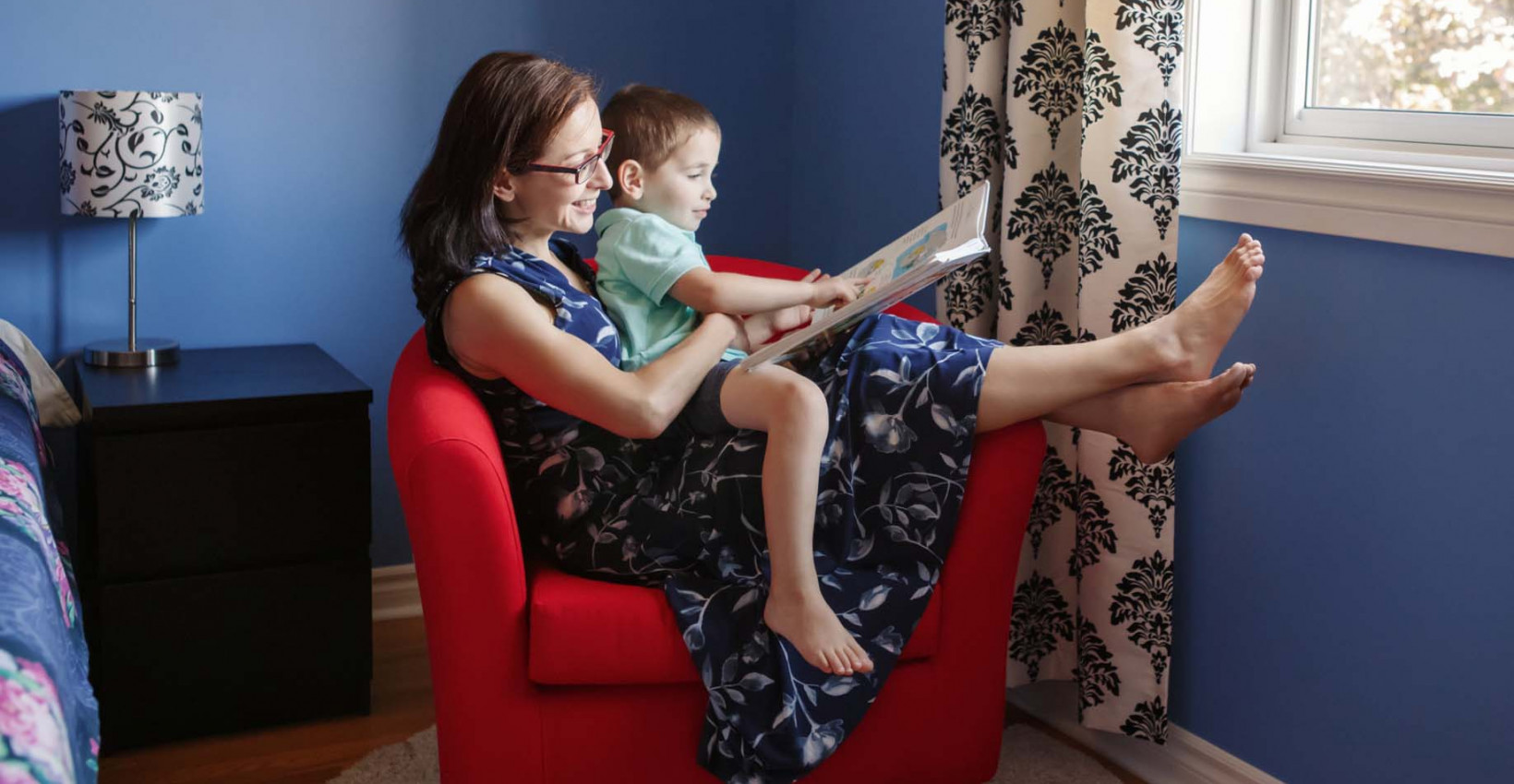 A mother and son reading a book by a window