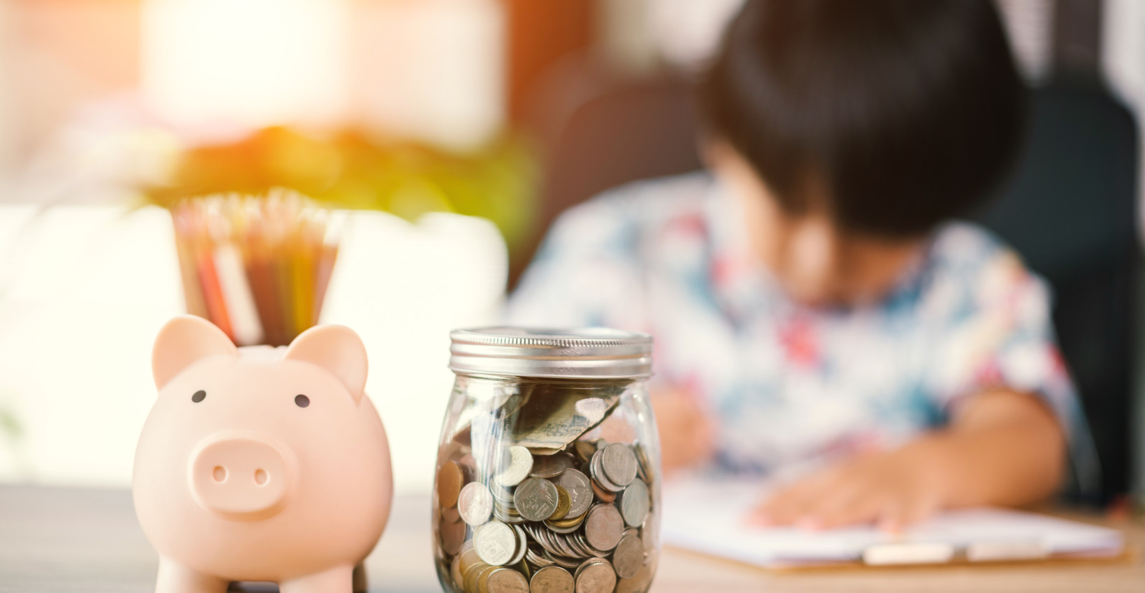 a small child sits at a table with a piggy bank and money