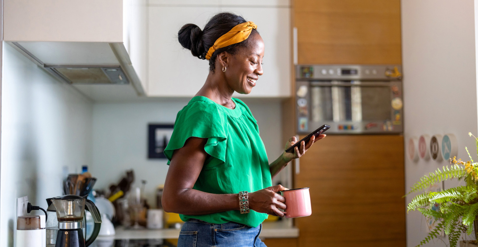 A woman holding a cup of coffee looking down at her phone
