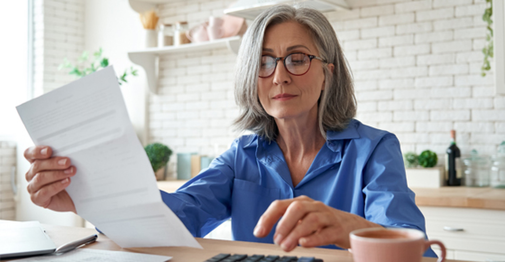a mature woman sits at a table reading a piece of paper