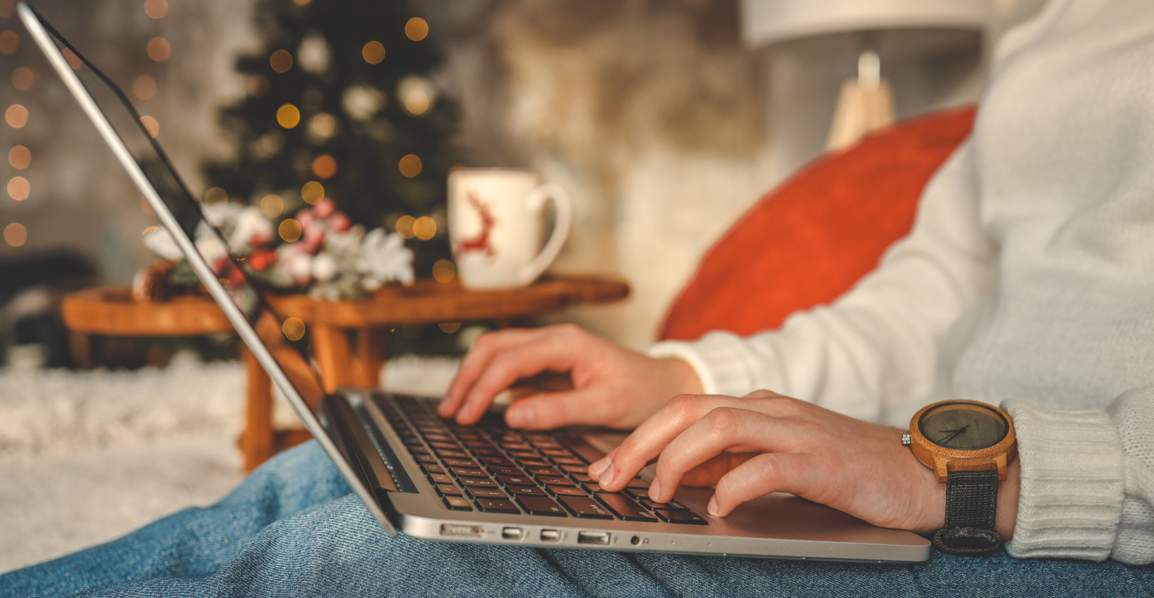 a person sits on a couch with a laptop on their lap with christmas decorations in the background