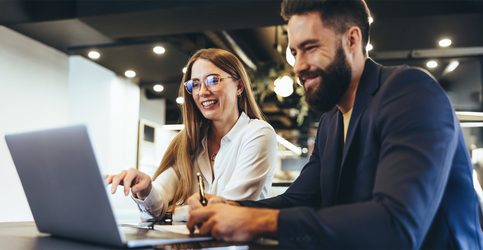a man and a woman sit at a table both looking at a laptop