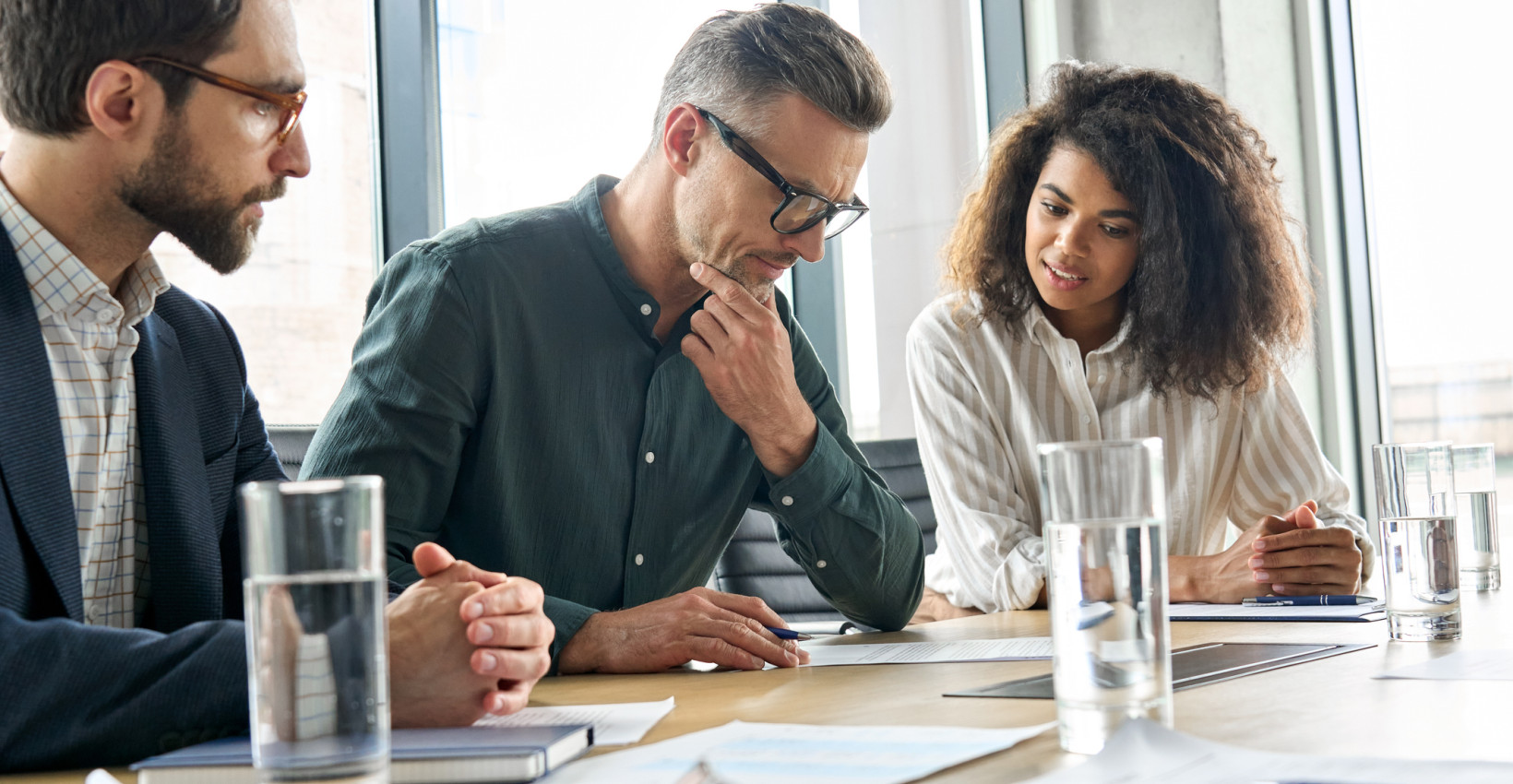 Three people look over notes at a meeting table