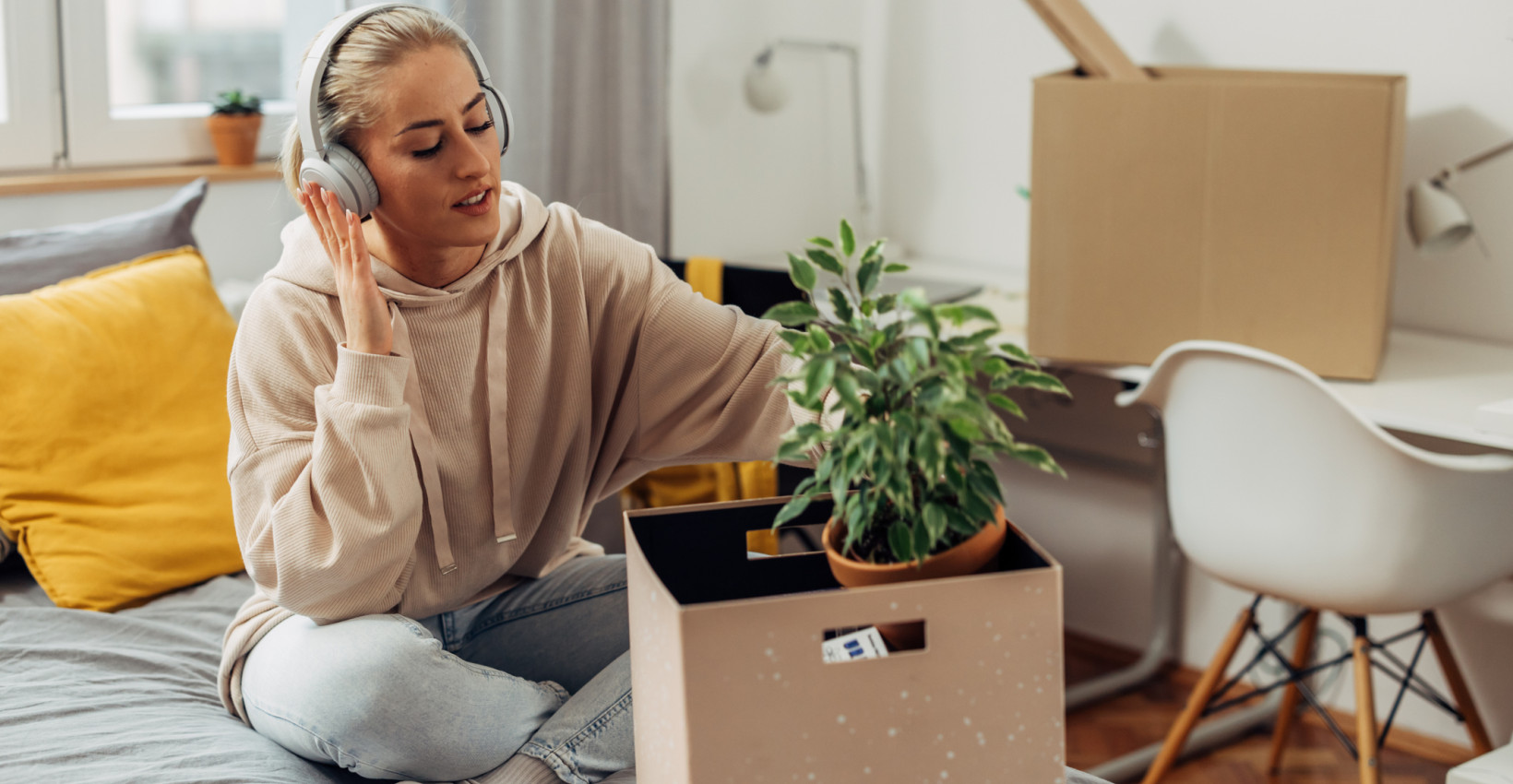 a younger female sits on a bed with headphones on looking through a box