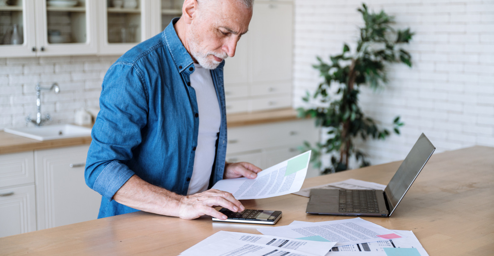 a man stands at a counter with his laptop and papers