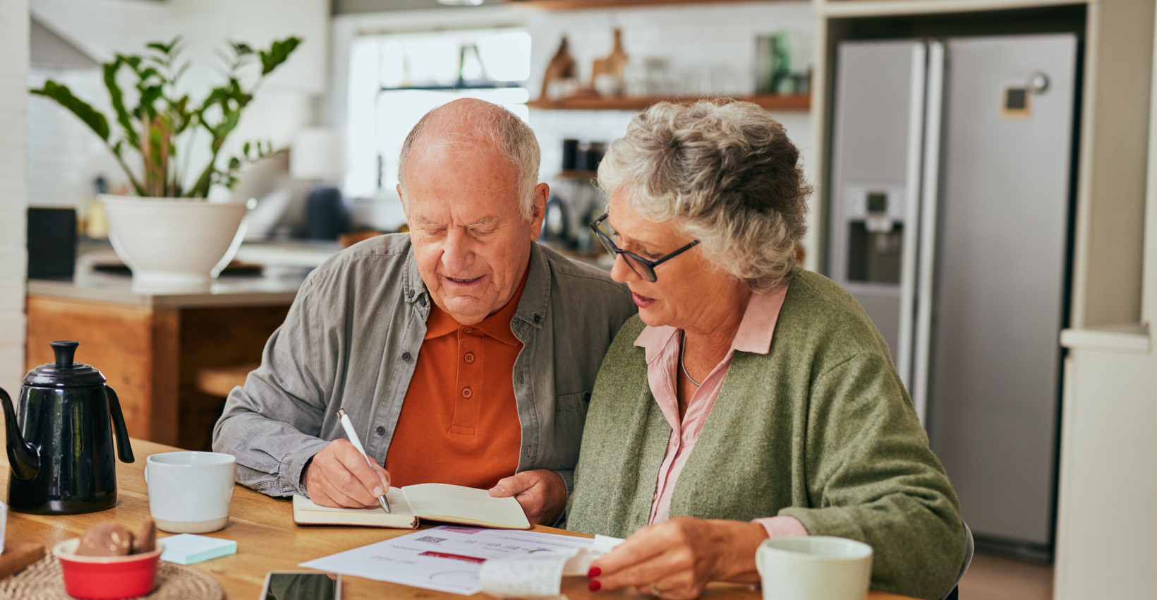 an elderly couple sits together at a table reviewing documents