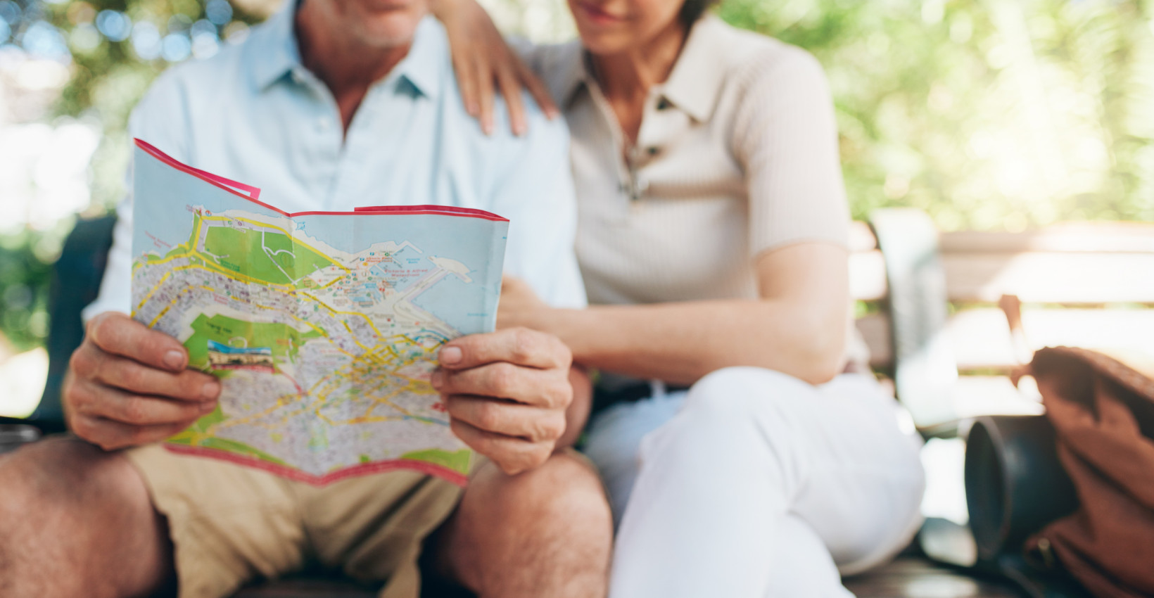 an older couple looks at a map while sitting on a park bench
