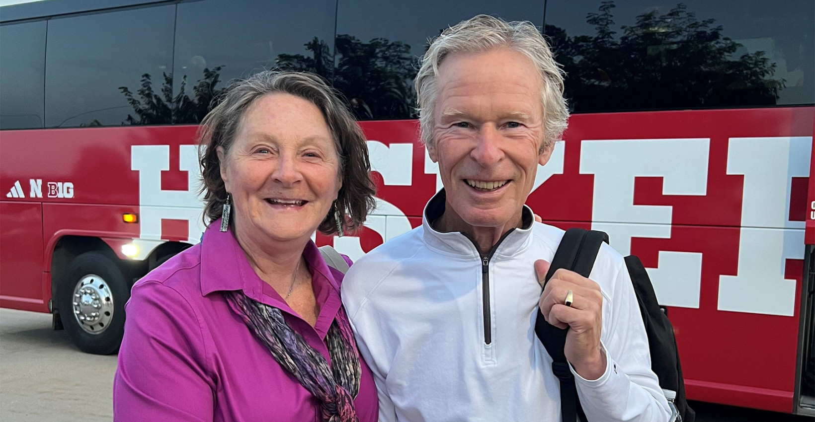 two people stand in front of a bus smiling
