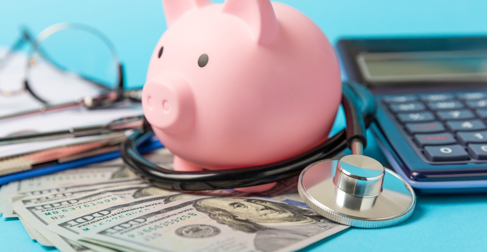 A piggy bank standing on cash next to a calculator