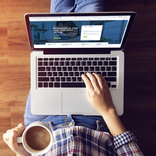 A person holding a cup of coffee and working on a laptop on their lap