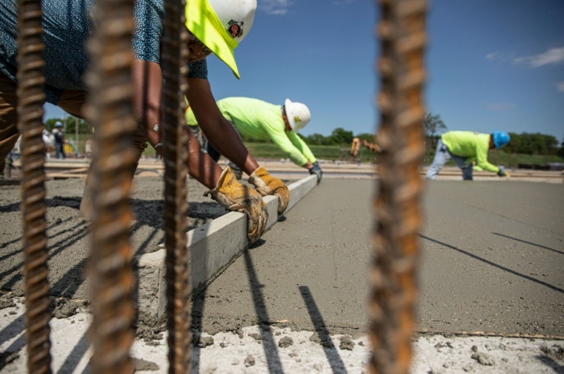 Construction workers pulling a level across freshly poured concrete