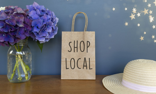 Shop local written on a paper bag with a hat and flowers.