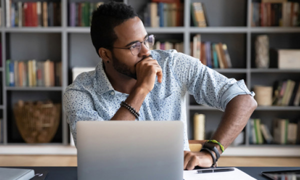 A man sitting behind his laptop looking off to the side lost in thought