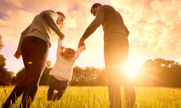 A couple swinging a child by the arms between them at sunset