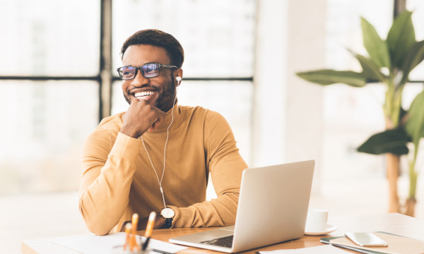 A man smiling as he sits at his home desk with a laptop