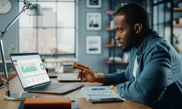 A man sitting at a wooden desk looking at charts on his computer. 