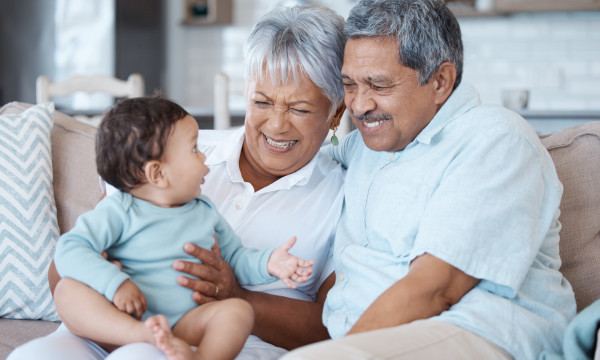 An elderly couple sitting on their couch with their infant grandchild. 