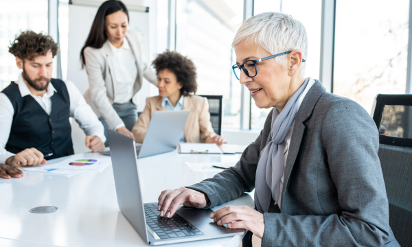 a woman sits at a computer at a conference table with other coworkers