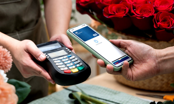 A person holds their phone near a card reader to pay with mobile wallet