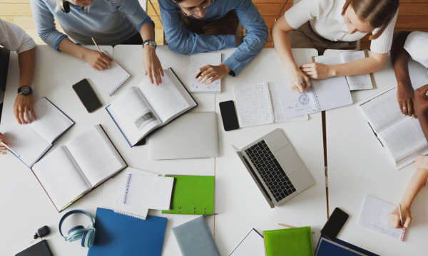 a group of people sit around a table with computers, papers, and pencils 