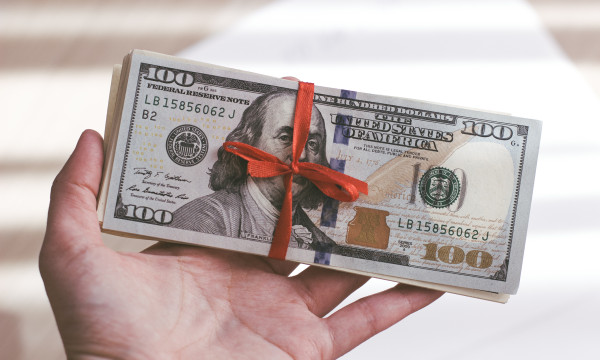 a hand holds a hundred dollar bill wrapped in red ribbon