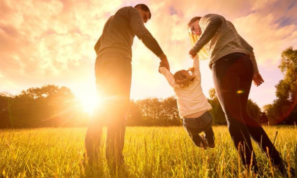 Parents lifting a kid up with a sunset in the background