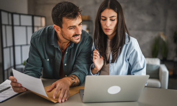 a man and a woman sit at a table with a laptop open
