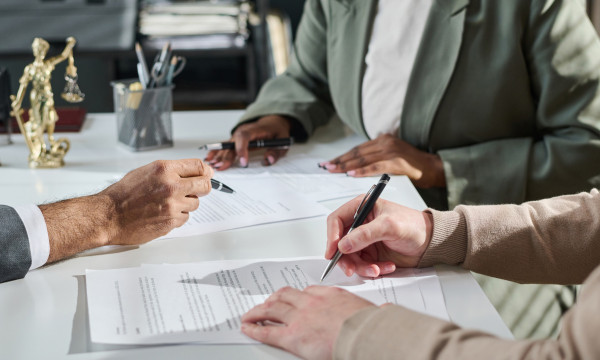 three people sit at a table looking at papers