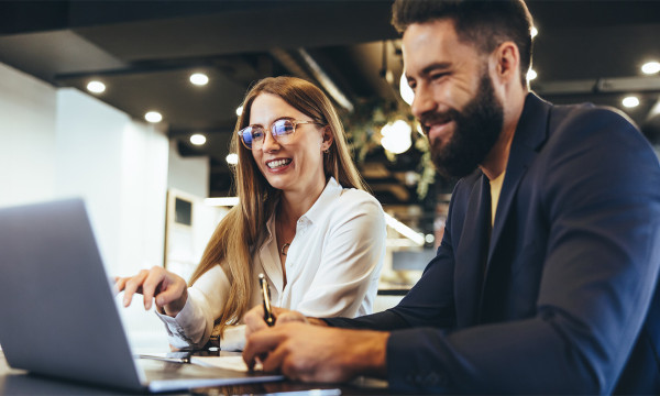  a man and a woman sit at a table both looking at a laptop