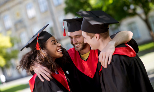 three college graduates stand together smiling