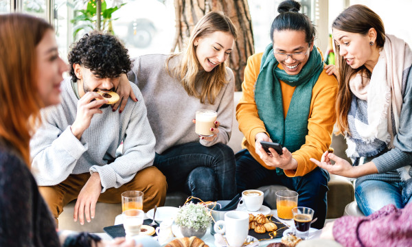 a group of 5 young people sit around a table with snacks and drinks laughing