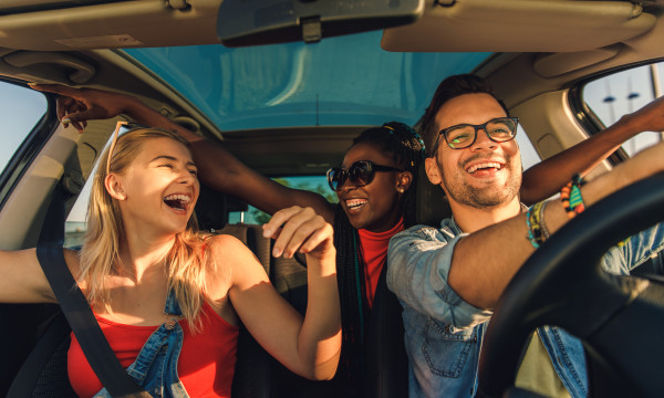 three younger people drive in a car together laughing