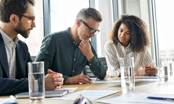 Three people look over notes at a meeting table