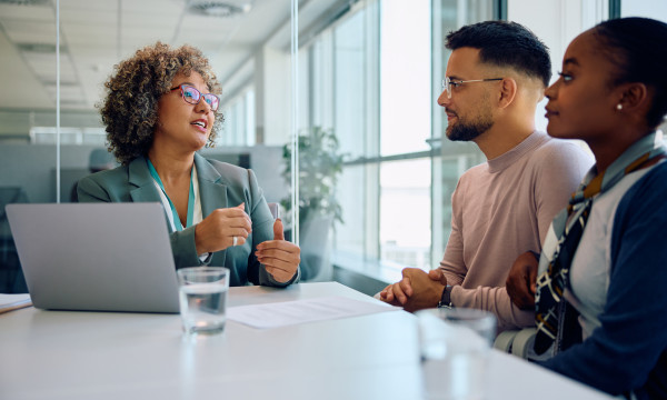 A couple sits at a table with a banker in front of her laptop
