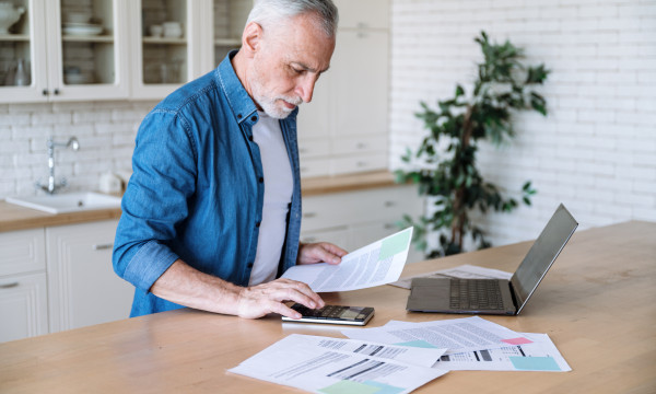a man stands at a counter with his laptop and papers
