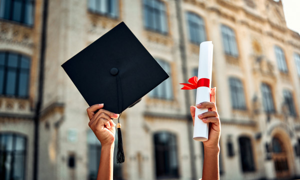 a person holds up a graduation hat and diploma wrapped in red ribbon