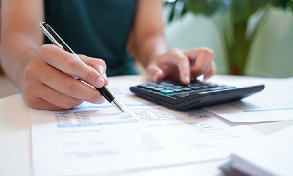 a woman writes on a paper with a calculator near by