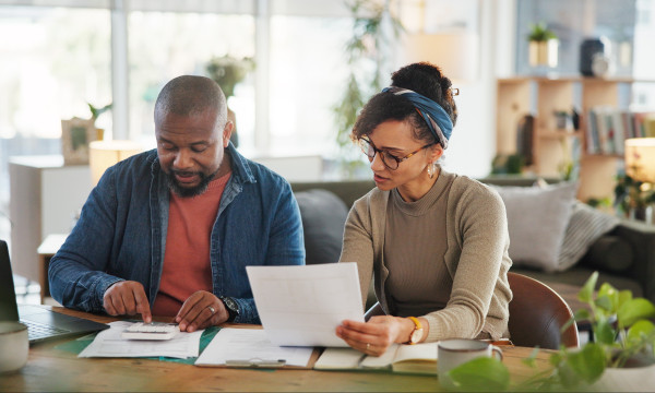 a black man and woman sit together at a table looking at paperwork in front of them