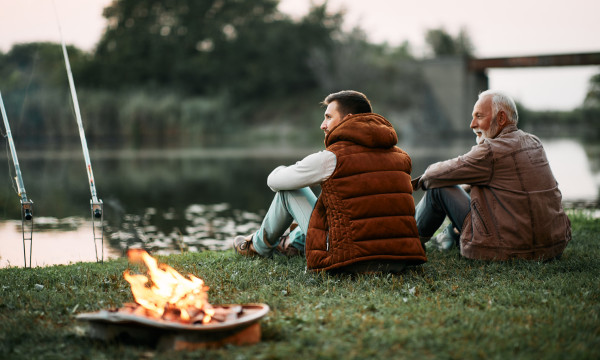 a dad and son sit together on the grass next to a fire