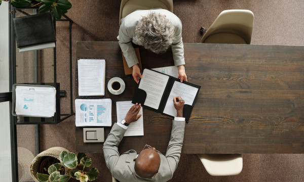 An overhead angle of two people having a meeting at a wooden table