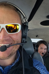 A selfie of a pilot in a small plane with a mother and young child behind him